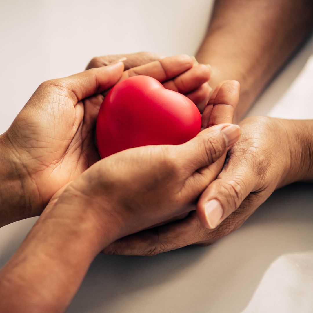 Mom and child with their hands touching, holding a red heart in the center of their hands. 